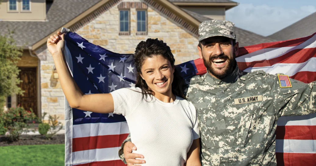 Military couple holding an American flag outside a home