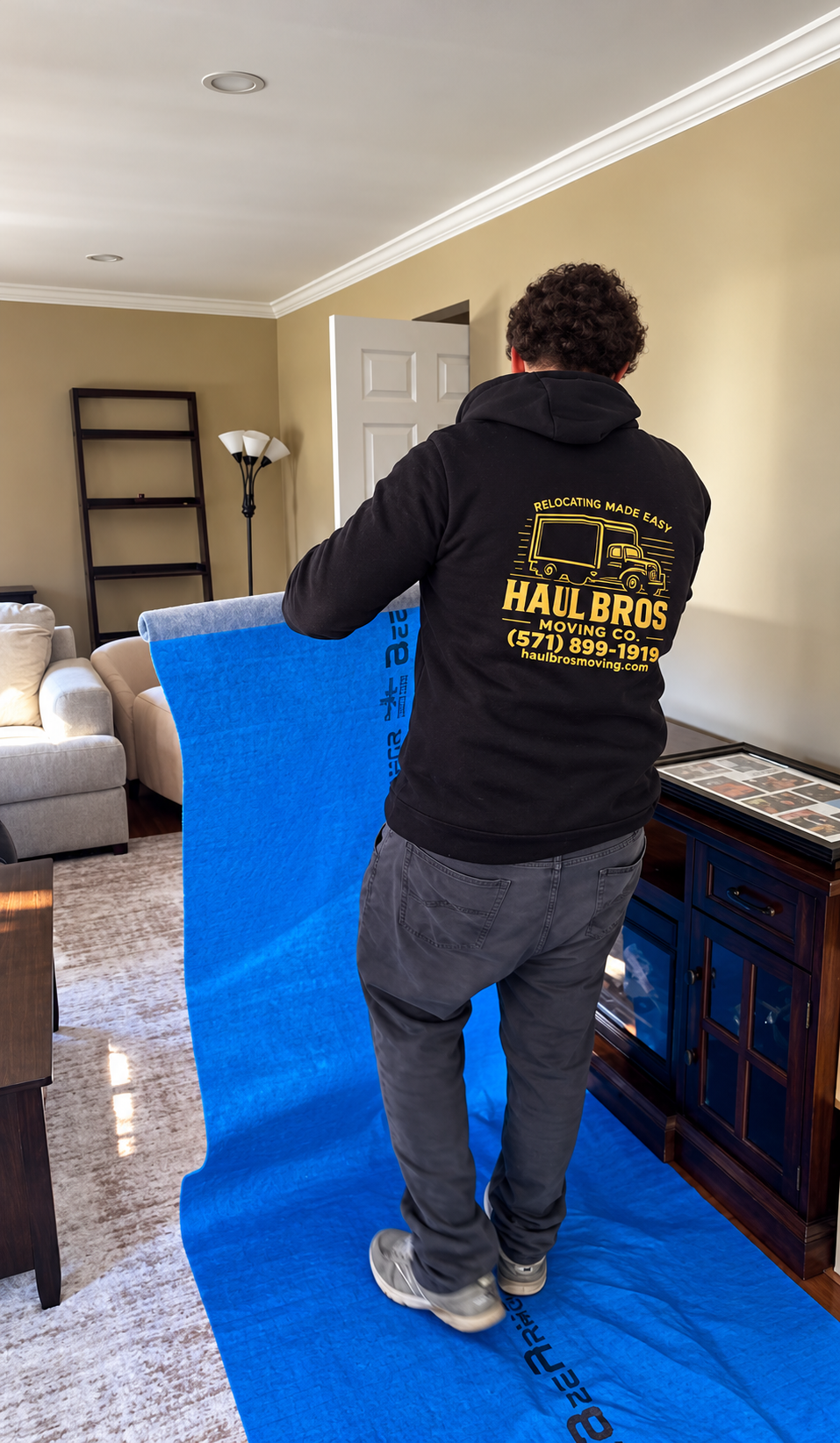 Haul Bros mover unrolling blue protective floor covering inside a home