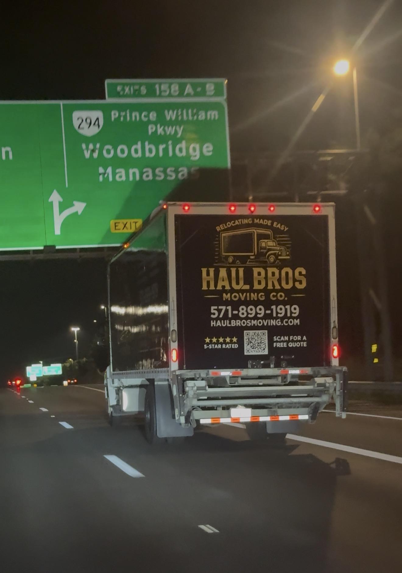 Haul Bros moving truck beneath a Woodbridge and Prince William Parkway highway sign at night